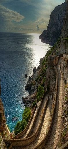 an aerial view of a road going down the side of a cliff by the ocean