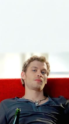 a man sitting in a red chair with a beer and looking at the camera while wearing a black shirt