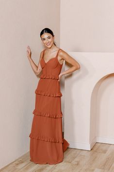 a woman standing in front of a wall wearing a brown dress