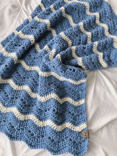 a blue and white crocheted blanket laying on top of a bed next to a pillow