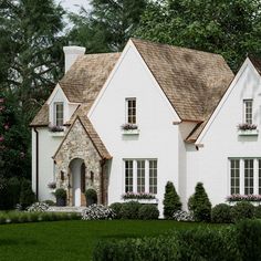 a white house surrounded by trees and flowers in the front yard with bushes around it