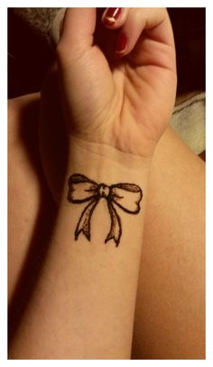 a woman's wrist tattoo with a bow on it