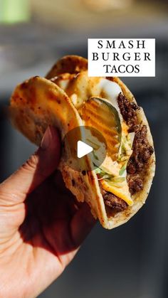 a hand holding up a sandwich with cheese and other toppings on it, in front of the words smash burger tacos