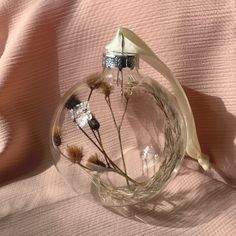 a glass vase filled with dried flowers on top of a pink cloth covered bed sheet