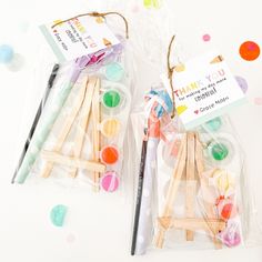 two small wooden clothes pins in plastic bags on a white surface with confetti scattered around them