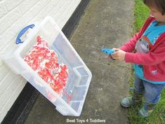 a young boy holding a pair of scissors next to a plastic container filled with red objects