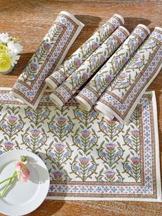 napkins and plates are laid out on a wooden table with flowers in the background