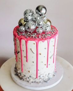 a white cake with pink icing and silver balls on top is sitting on a table