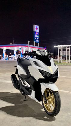 a white and black motorcycle parked in front of a gas station at night with the lights on