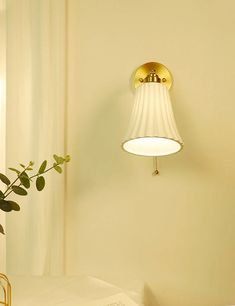 a lamp that is on the wall next to a table with a plant in it