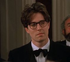 the young man is wearing glasses and a tuxedo in front of an older gentleman