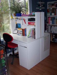 a white desk with books on it and a red chair in front of the window