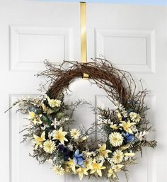 a wreath hanging on the front door with flowers and foliage around it, as well as a gold ribbon