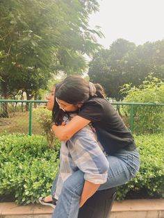 two people hugging each other in front of some bushes