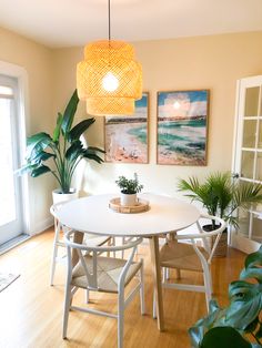 a white table and chairs in a room with plants on the floor, paintings on the wall