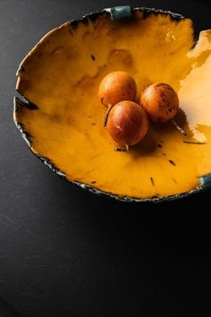 three oranges in a yellow bowl on a black table