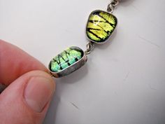 a person is holding onto a green and yellow bracelet that has two leaves on it