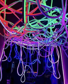 neon colored wires hang from the ceiling in a dark room