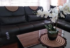 a living room with black leather couches and white flowers in a vase on the coffee table