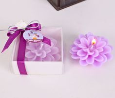 a purple flower sitting next to a candle in a white box with a purple ribbon