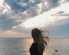 a woman standing on top of a beach next to the ocean under a cloudy sky