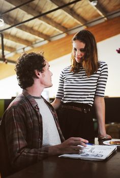 a woman standing next to a man sitting at a table in front of a book