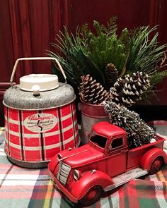 an old fashioned red truck with pine cones in the back sits on a plaid tablecloth