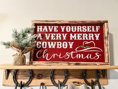 a wooden sign that says have yourself a very merry cowboy christmas with horseshoes hanging from hooks