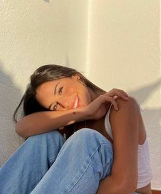 a beautiful young woman sitting on top of a wooden floor next to a white wall