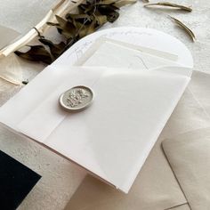 a white envelope with a wax stamp on it next to some dried flowers and leaves