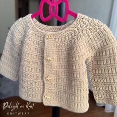 a knitted sweater with pink bows hanging on a clothes hanger in front of a door