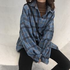 a woman sitting on top of a white wall wearing black pants and a blue plaid shirt