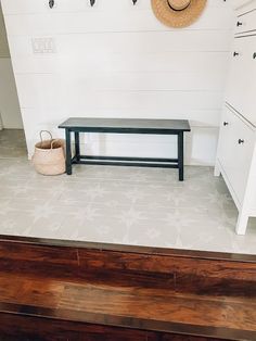 there is a bench and hat on the floor in this room with white walls, wood floors and cabinets