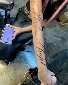 a woman sitting on the floor with her cell phone in her hand and writing on her arm