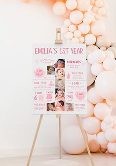 a pink and white baby's first year sign next to balloons in the background