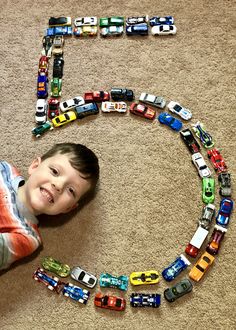 a young boy laying on the floor next to a number made out of toy cars