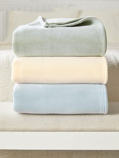 three sheets stacked on top of each other in front of a white bed with pillows