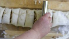 a hand holding a metal object in front of some dough on a wooden surface with other items behind it