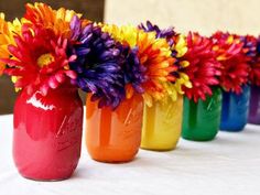 colorful vases with flowers in them lined up on a table