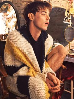 a man sitting in a chair wearing a yellow and black sweater with his hands on his knees