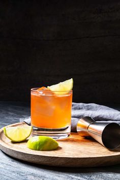 an orange drink with limes on the side and a cocktail shaker next to it