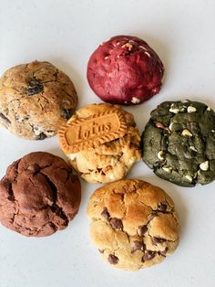 six cookies with different flavors on a white surface, including one cookie and the other chocolate chip