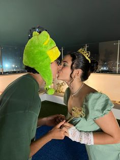 a man and woman kissing each other in front of a stuffed frog on top of a bed