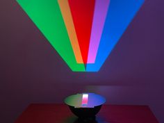 a bowl sitting on top of a wooden table under a rainbow colored ceiling light in a room