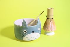 a blue and white cat cup next to a wooden brush holder on a yellow background