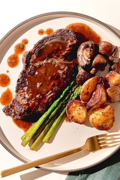 a white plate topped with meat, potatoes and asparagus on top of a table