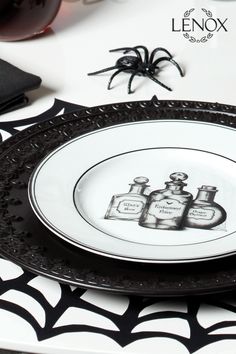 a black and white plate with two bottles of perfume on it next to a spider