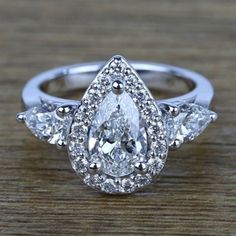 three pear shaped diamond engagement rings on top of a wooden table