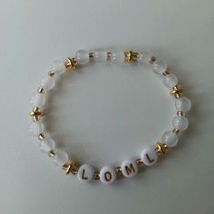 a white beaded bracelet with gold beads and the word lom written on it