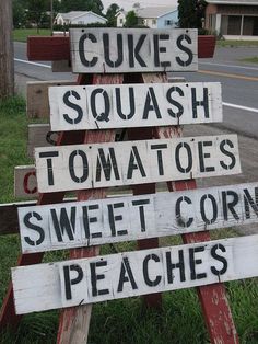 a wooden sign sitting on the side of a road that says cukes squash tomatoes sweet corn peaches